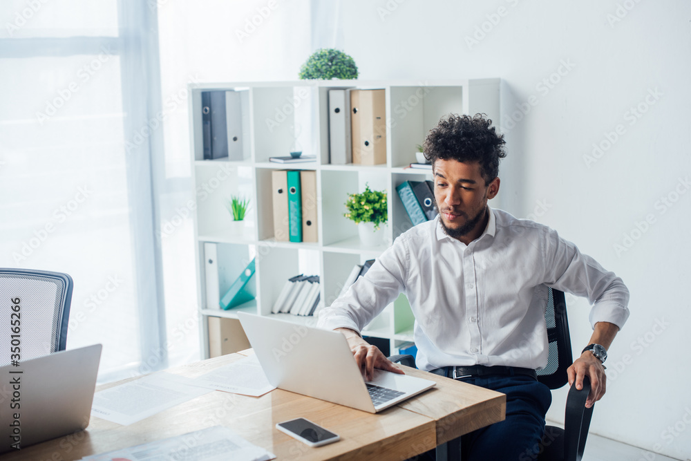 African american businessman using laptop near papers on table African american businessman using laptop near papers on table