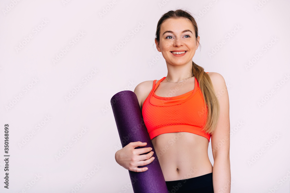 Portrait of smiling young attractive girl holding a yoga mat ove