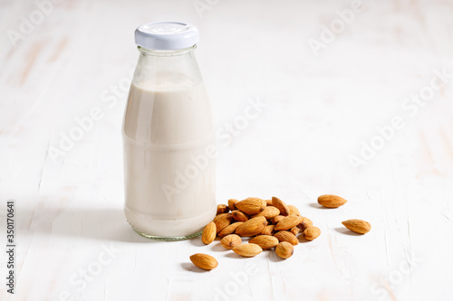 Almond milk in glass bottle with fresh almond nuts