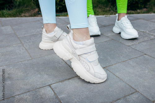 White sneakers on two girls legs on the asphalt background