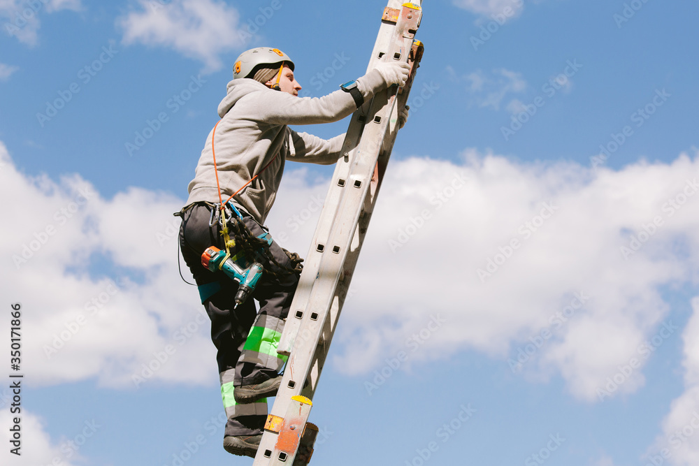 Industrial climber in helmet and overall working on height. Risky job. Professional worker going up the ladder.
