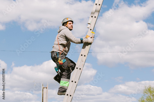 Industrial climber in helmet and overall working on height. Risky job. Professional worker going up the ladder.