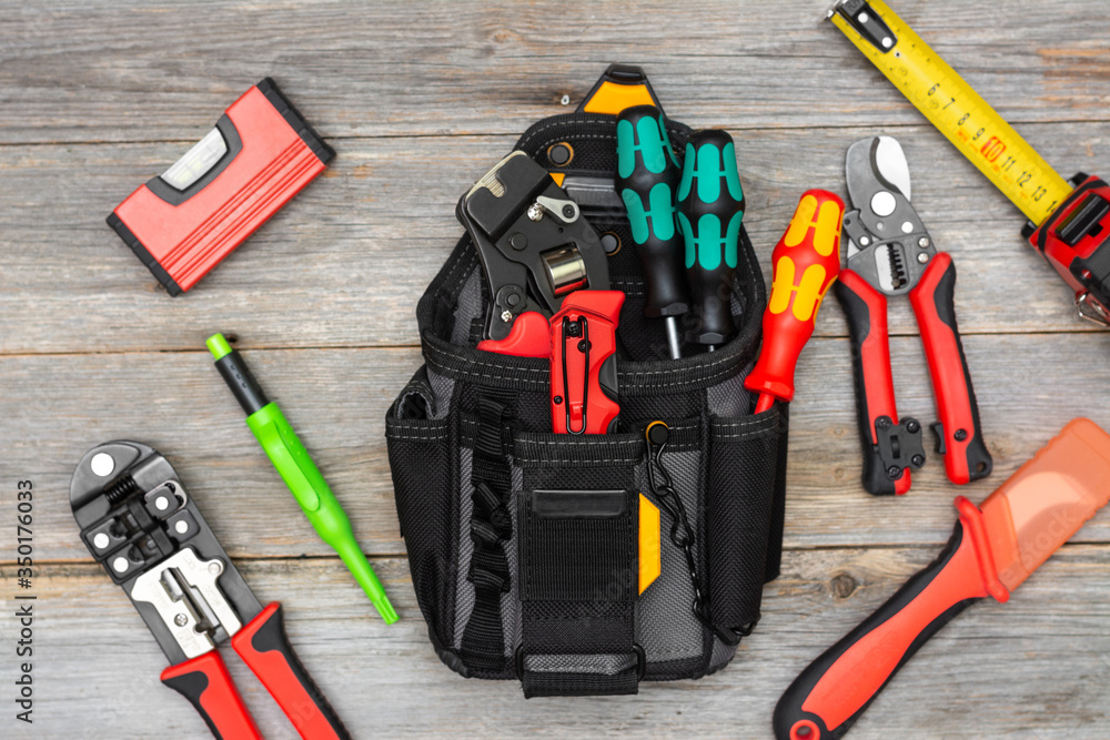Electrician's tools on a gray wooden table. Bag with construction tools for electrical installation. Crimping, screwdrivers, wire cutters, construction tape measure on the table Electrician's tools on a gray wooden table. Bag with construction tools for electrical installation. Crimping, screwdrivers, wire cutters, construction tape measure on the table