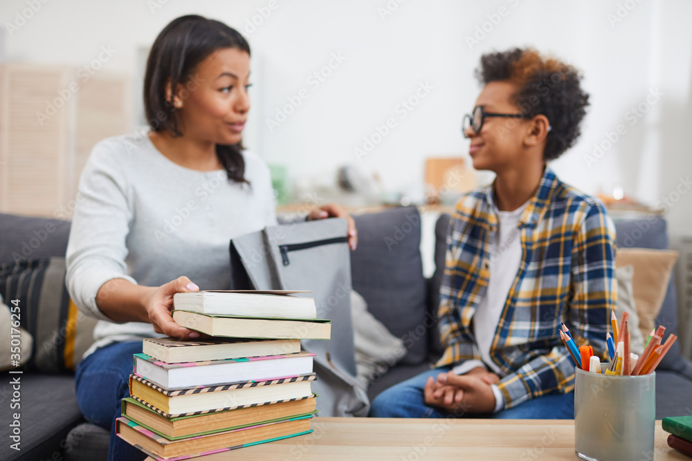 Obraz premium Portrait of young African-American woman talking to son while holding books for homeschooling, focus on foreground, copy space