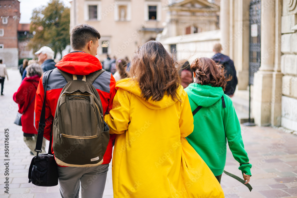 Three young people tourists from behind in colored clothes as a traffic light (red, green yellow) walk, communicate, rest and travel