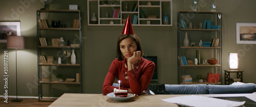 Upset girl wearing party hat celebrating her birthday alone during quarantine. Stay home, self isolation, quarantine life. Shot with anamorphic lens photo