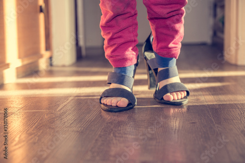 Detail view of young girl walking in her mother high heel shoes.