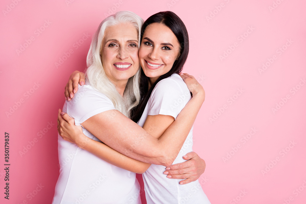 Photo of charming aged mother young pretty daughter two ladies hugging cozy best friends finally together wear casual white t-shirts isolated pastel pink color background Photo of charming aged mother young pretty daughter two ladies hugging cozy best friends finally together wear casual white t-shirts isolated pastel pink color background