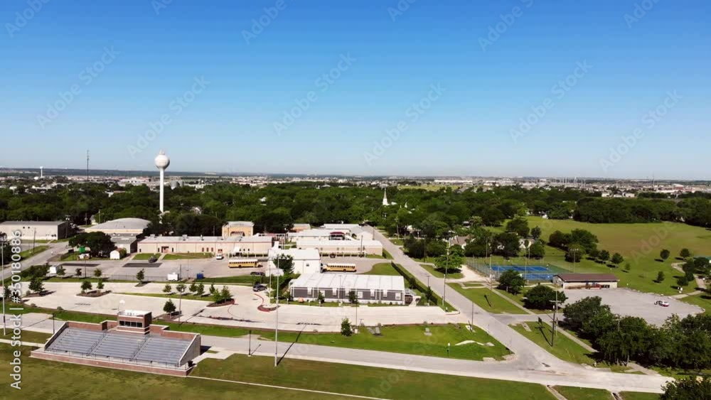 Flying back across a portion of football field near one end of the field, good view of the city's parks and rec department. Couple of school buses, water towers are visible along with tennis courts. Flying back across a portion of football field near one end of the field, good view of the city's parks and rec department. Couple of school buses, water towers are visible along with tennis courts.