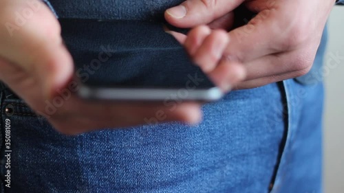 A young European man takes a phone from his pocket and swings a finger over it, then puts it back in his pocket. Close-up.