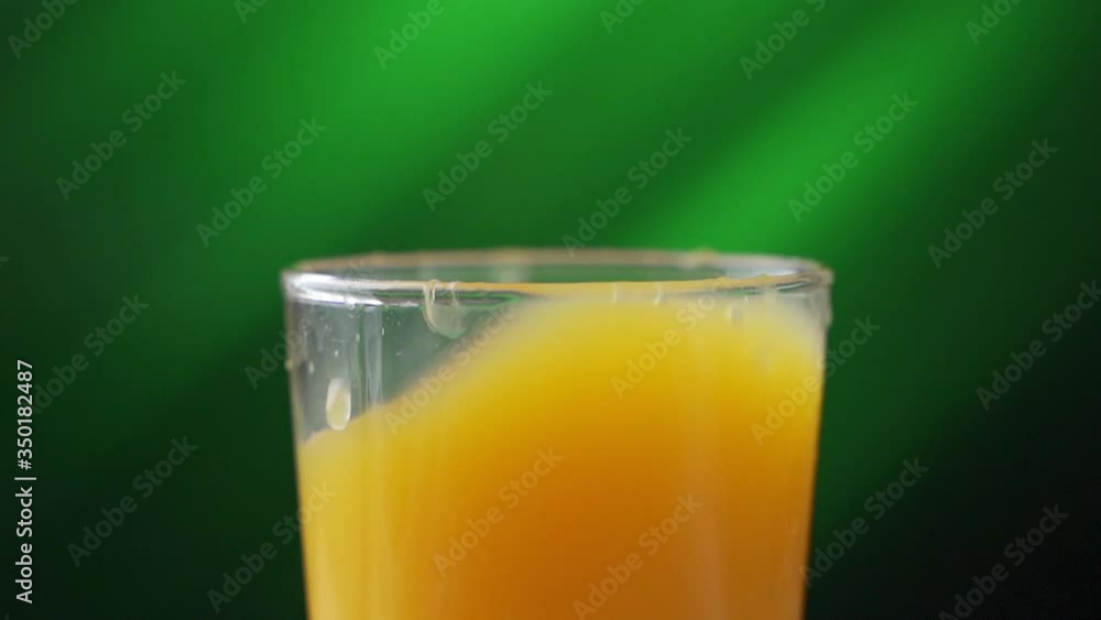 Glass with orange juice. Ice cube fall, creating a lot of splashing. Slow motion Glass with orange juice. Ice cube fall, creating a lot of splashing. Slow motion