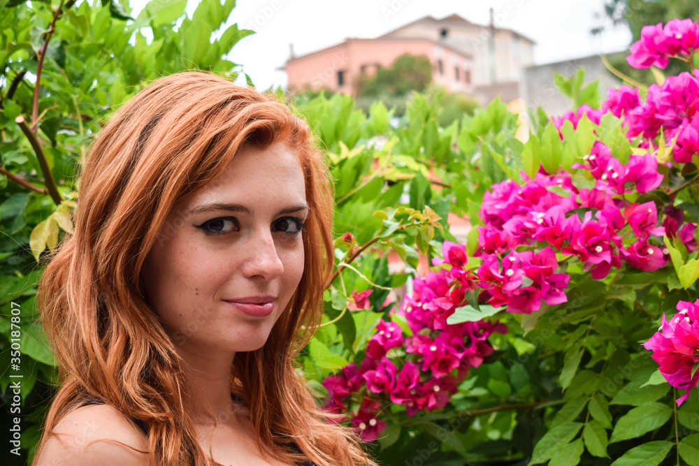 Naklejka premium Orange hair girl with violet Bougainvillea in the background of the garden