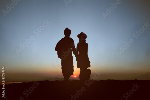 Silhouette of a couple in a hat with backpack and suitcase traveling