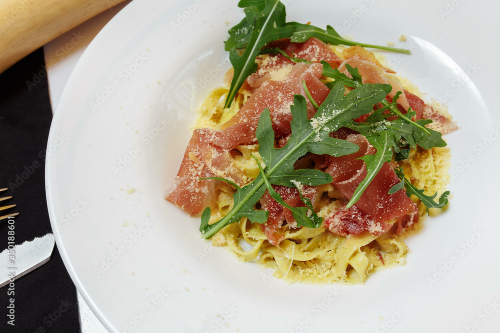 Tasty Italian pasta appetizer with basturma and fresh basil on top on a white table background with docures Tasty Italian pasta appetizer with basturma and fresh basil on top on a white table background with docures