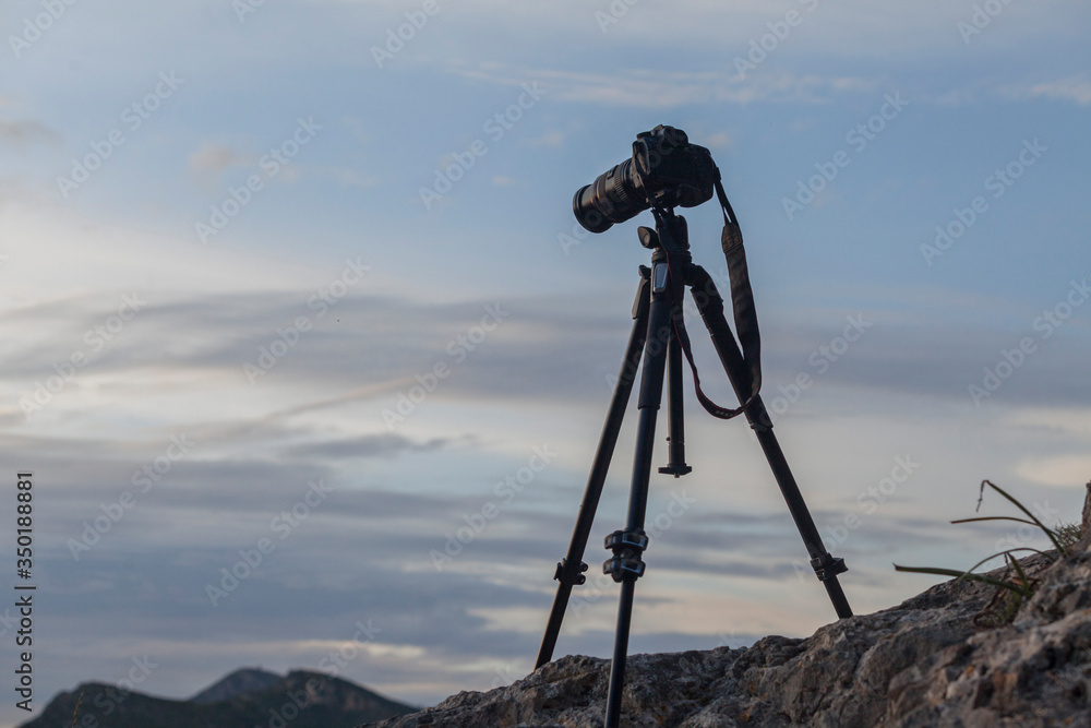 A photo camera on a tripod in mountainous background at sunset. Mallorca.Spain. A photo camera on a tripod in mountainous background at sunset. Mallorca.Spain.