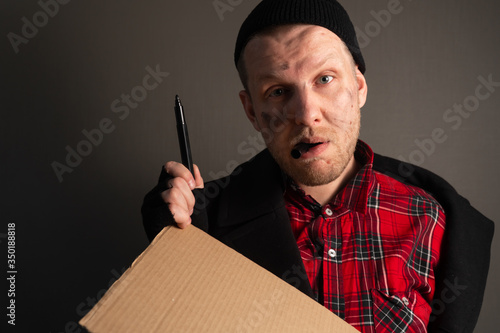 portrait a young man who holds a felttip pen in his mouth to write text on cardboard. begging concept photo