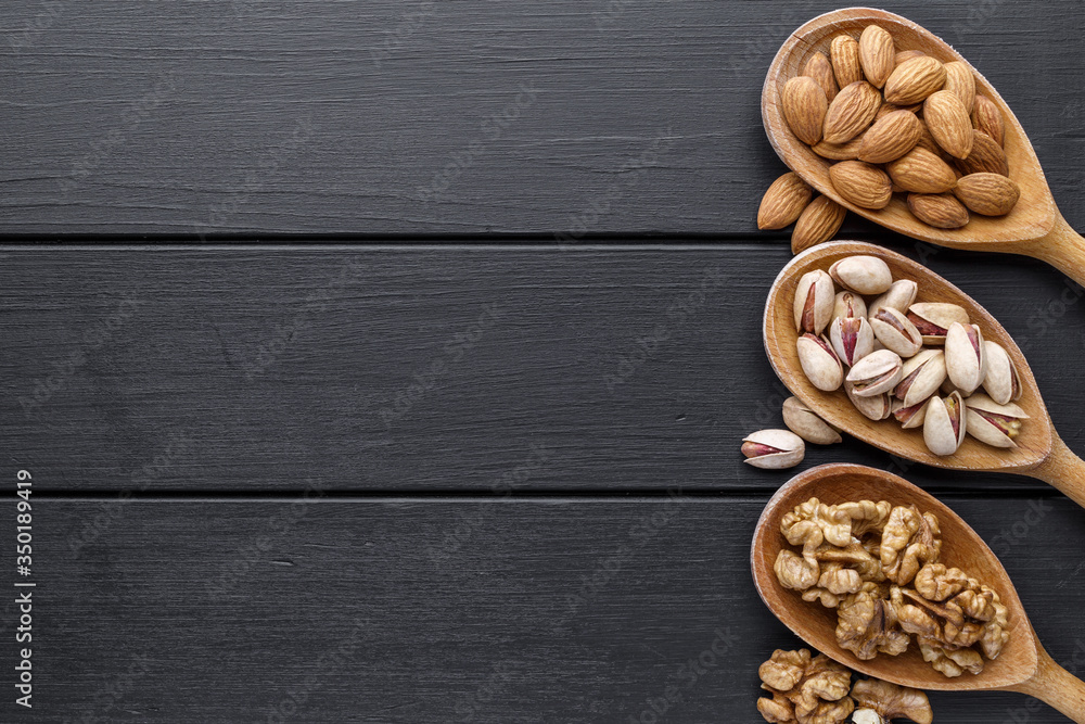 nuts in wooden bowl. Assortment of nuts - cashew, hazelnuts, walnuts, pistachio, pecans, pine nuts, peanut, raisins on black background.Healthy snack, vegetarian food, Top view. nuts in wooden bowl. Assortment of nuts - cashew, hazelnuts, walnuts, pistachio, pecans, pine nuts, peanut, raisins on black background.Healthy snack, vegetarian food, Top view.