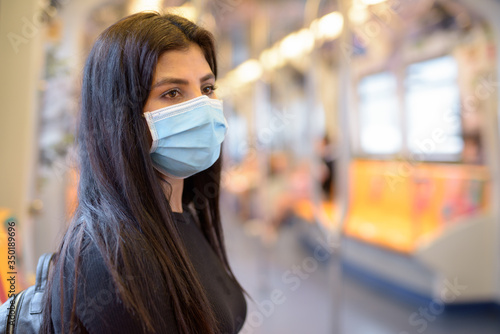 Young Indian woman with mask for protection from corona virus outbreak sitting with distance inside the train