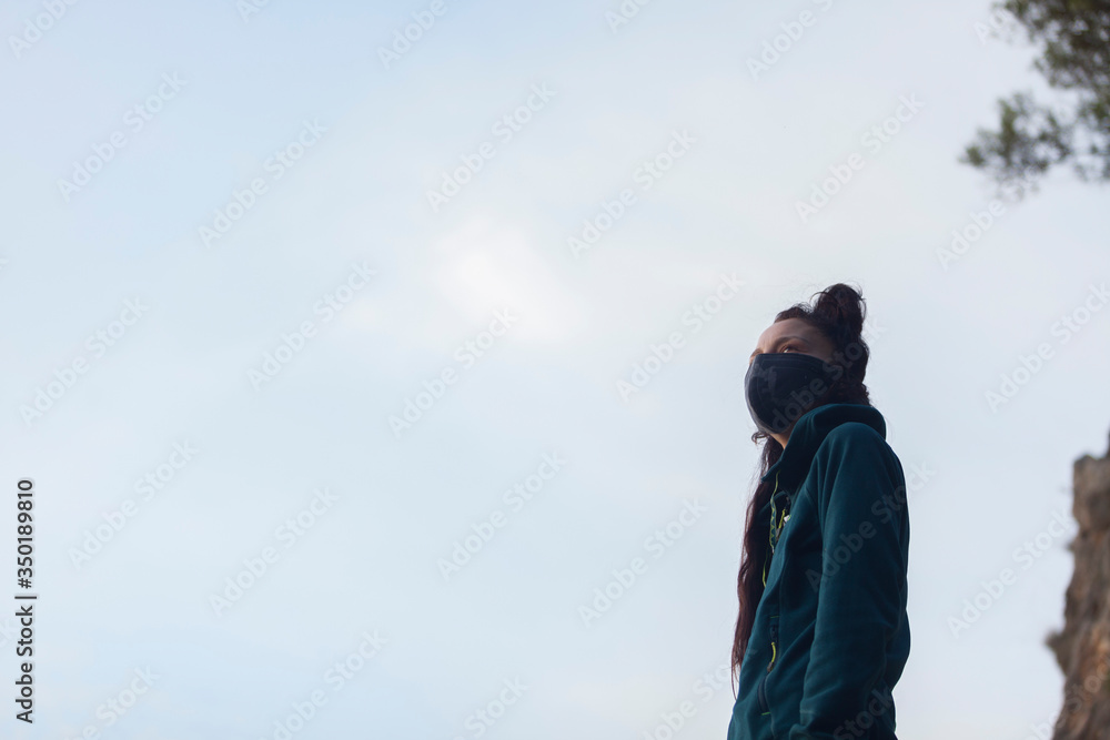 A woman with a mask on a blue sky background during the coronavirus pandemic. New normal