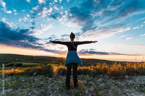Young woman looks at the sun and the sky with open arms.