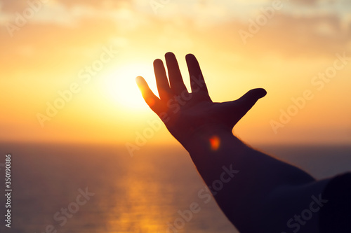 Canvas Print young man raising hands praying at sunset or sunrise light, dreams, freedom and