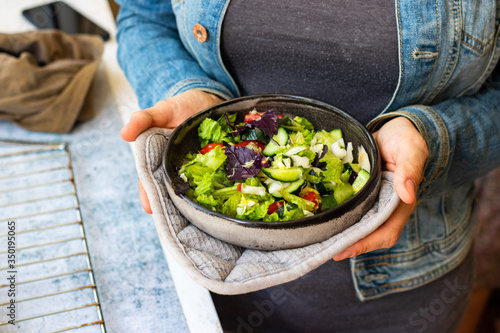 Green vegetables salad with basil, lettuce, cucumber, tomatoes. Vegan healthy food. Woman hands