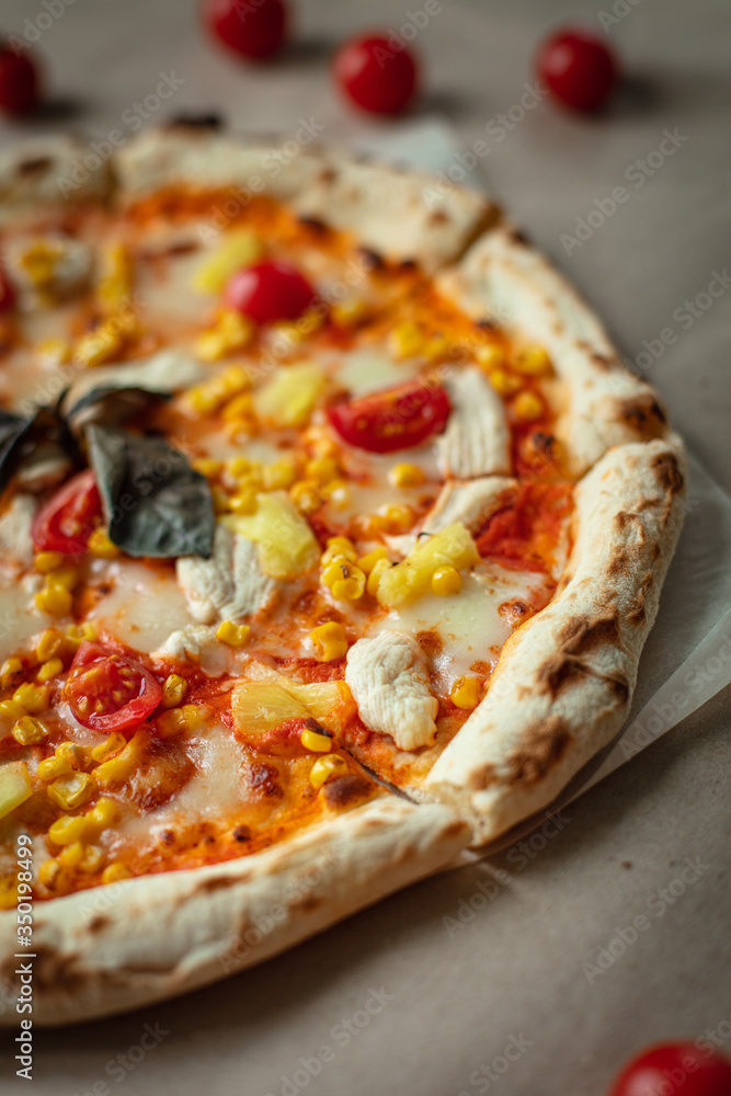 Pizza closeup with chicken, tomatoes, pineapple, cheese on Kraft paper or wood. Fresh pizza.