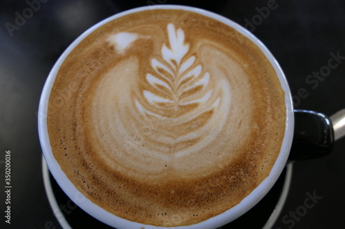 Caffe latte or cappuccino similar to flat white with leaf pattern in milk foam, coffee culture and art in one