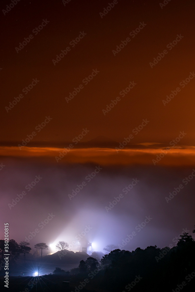 Mountains in fog at beautiful night in autumn in Dalat city, Vietnam. Landscape with Langbiang mountain valley, low clouds, forest, colorful sky with stars, city illumination at dusk. Mountains in fog at beautiful night in autumn in Dalat city, Vietnam. Landscape with Langbiang mountain valley, low clouds, forest, colorful sky with stars, city illumination at dusk.