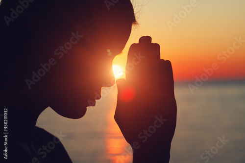 silhouette of young woman raising hands praying at sunset or sunrise light, practicing yoga on the beach, religion, freedom and spirituality concept