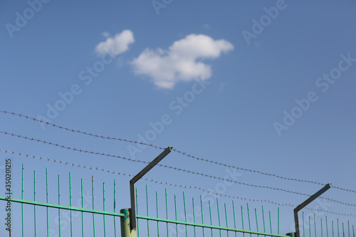 Lonely cloud in blue sky behind barbed wire