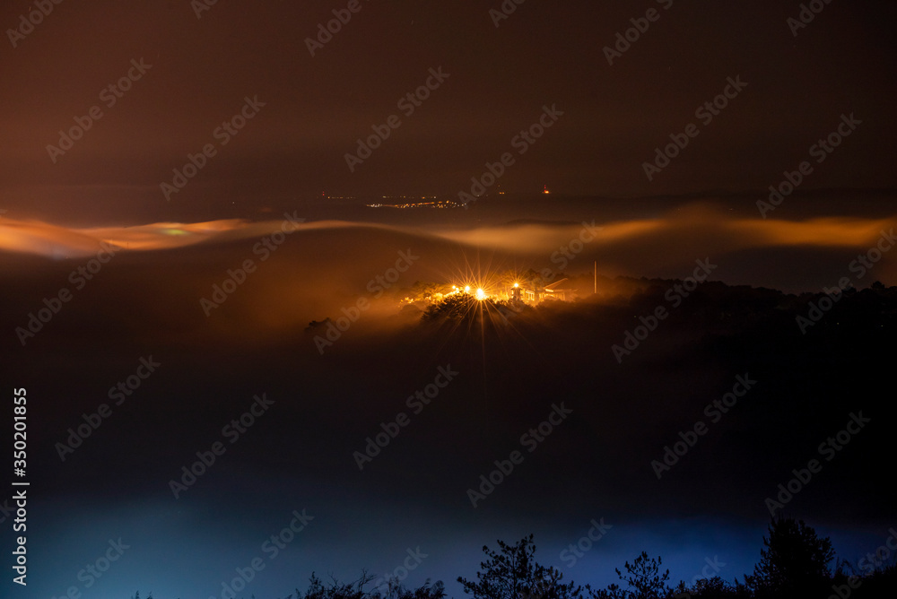Mountains in fog at beautiful night in autumn in Dalat city, Vietnam. Landscape with Langbiang mountain valley, low clouds, forest, colorful sky with stars, city illumination at dusk. Mountains in fog at beautiful night in autumn in Dalat city, Vietnam. Landscape with Langbiang mountain valley, low clouds, forest, colorful sky with stars, city illumination at dusk.