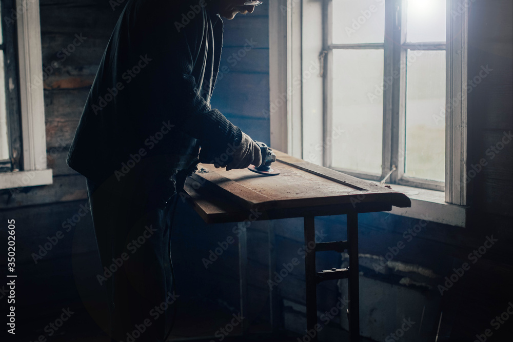 Fototapeta premium elderly man polishes a wooden board with a grinder at home. Furniture restoration, housework.