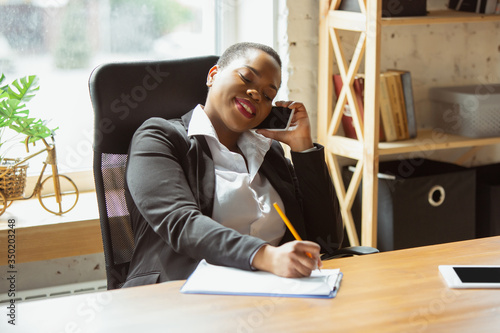 Business call. African-american businesswoman in office attire smiling, looks confident and happy, busy. Finance, business, equality and human rights concept. Beautiful young feme model, successful. photo
