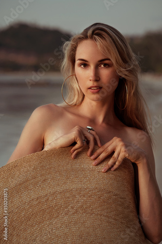 Obraz na płótnie portrait of a blond girl covered herself with a big straw summer hat on the beach and looking at camera w salonie