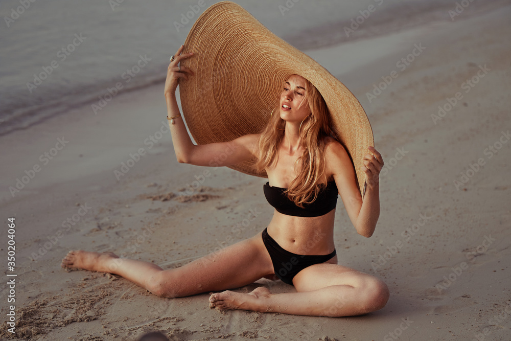 portrait of blonde girl wearing big straw summer hat enjoying sunset
