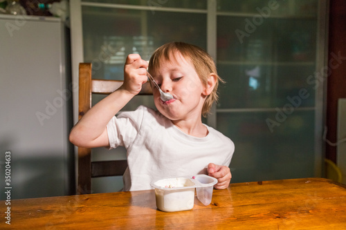 Adorable baby girl eating cottage cheese from spoon, healthy milk snack. 