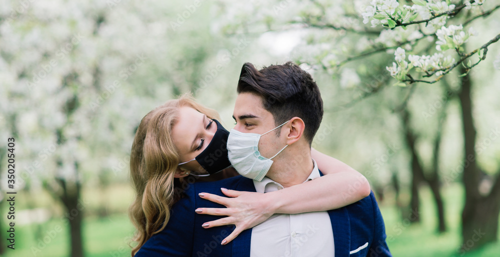 Young loving couple walking in medical masks in the park during quarantine on their wedding day. Coronavirus, disease, protection, sick, illness flu europe celebration canceled. Young loving couple walking in medical masks in the park during quarantine on their wedding day. Coronavirus, disease, protection, sick, illness flu europe celebration canceled.