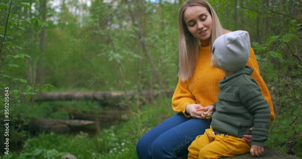 Mother and son sitting on a log of a tree in the forest near the stream ...