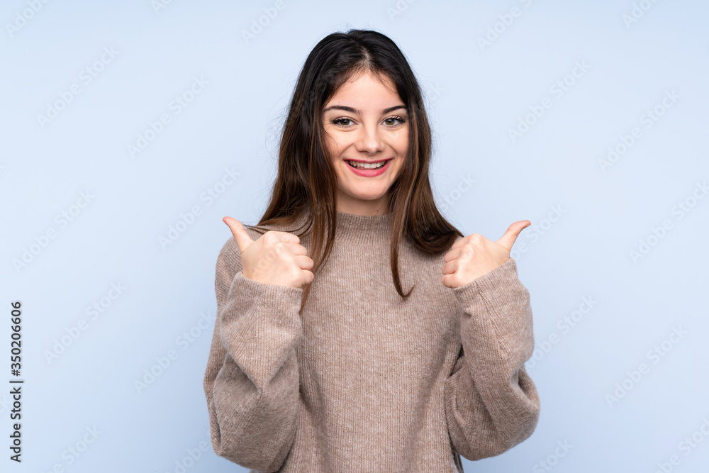 Young brunette woman wearing a sweater over isolated blue background with thumbs up gesture and smiling Young brunette woman wearing a sweater over isolated blue background with thumbs up gesture and smiling
