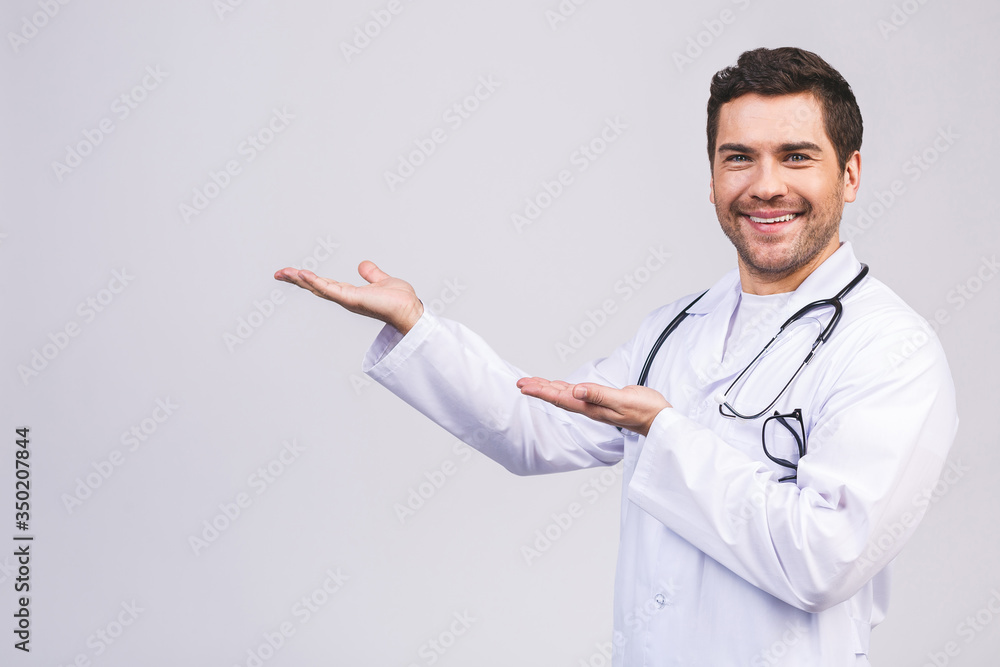 Young smiling doctor man, medical professional holding something in empty hand isolated over white background. Pointing finger. Young smiling doctor man, medical professional holding something in empty hand isolated over white background. Pointing finger.