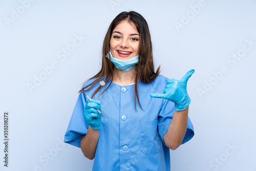 Woman dentist holding tools over isolated blue background making phone gesture