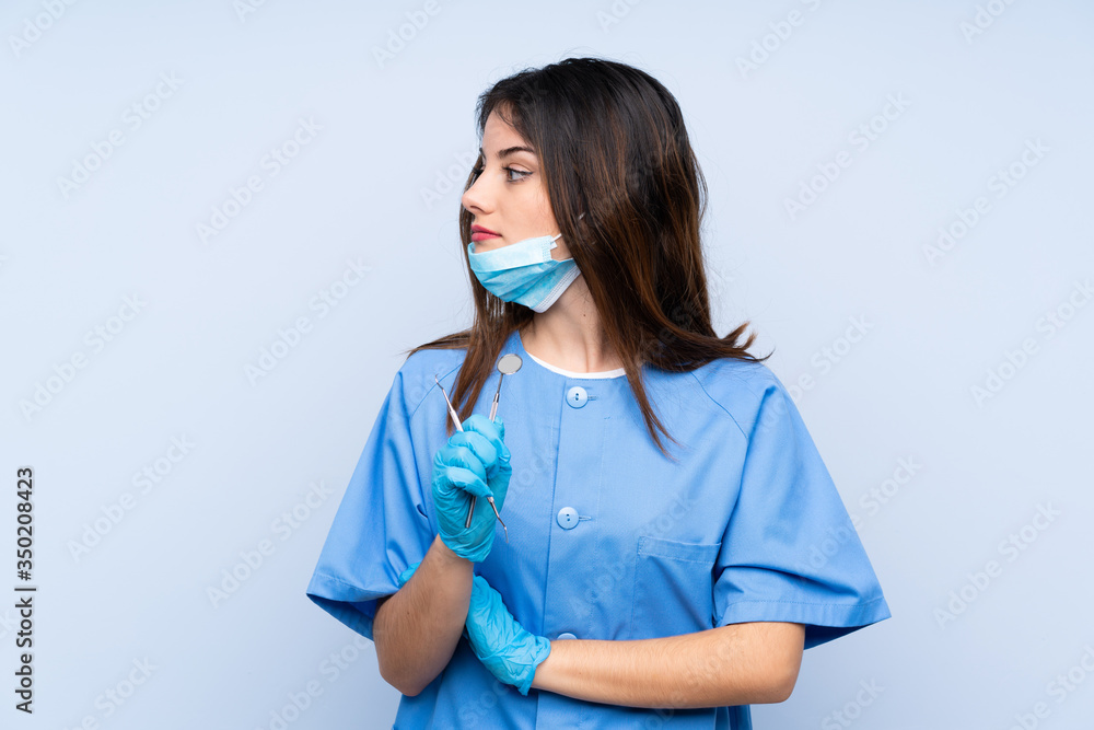 Woman dentist holding tools over isolated blue background looking side Woman dentist holding tools over isolated blue background looking side