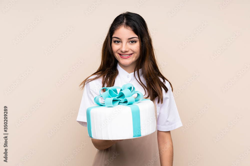 Pastry chef woman holding a big cake over isolated background smiling a lot Pastry chef woman holding a big cake over isolated background smiling a lot