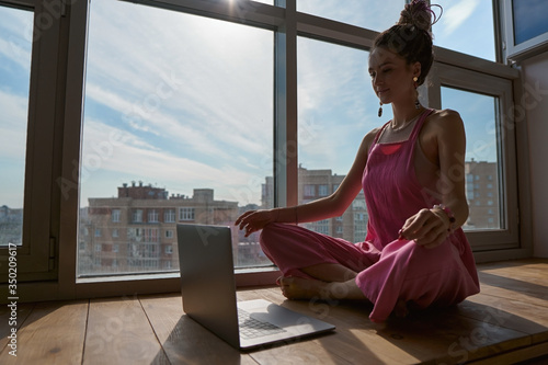 Beautiful brunette girl in pink clothes sitting on the windowsill and working from home. freelanser concept