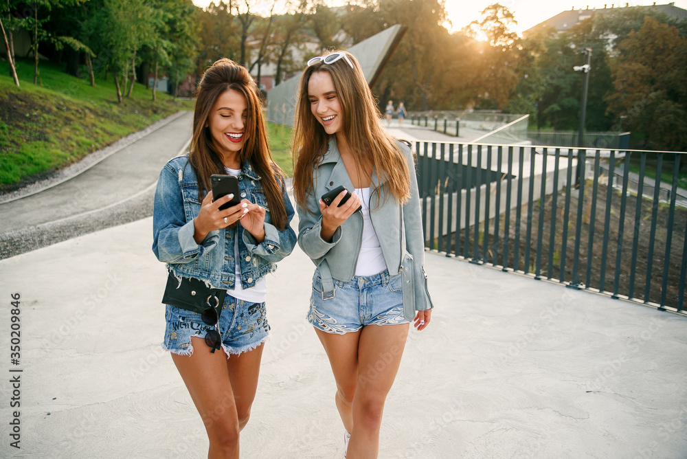Girlfriends uses smartphone while walking in the city at morning. Female top bloggers travels in europe city. Modern communication smart technologies and friendship concept.