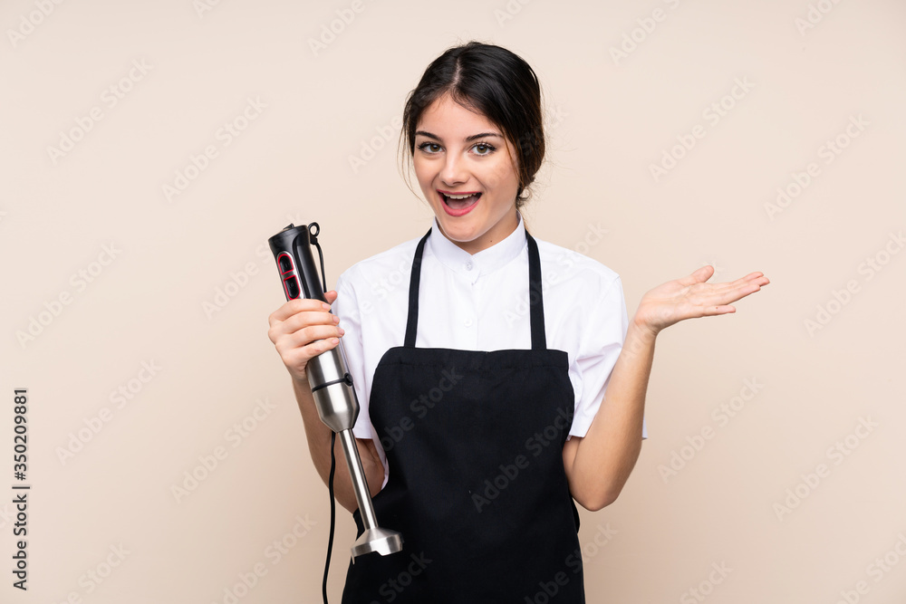 Young woman using hand blender over isolated background with shocked facial expression