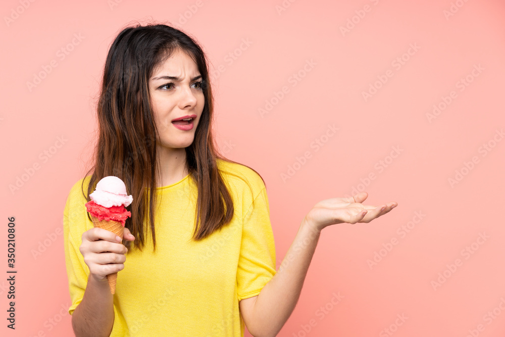Young brunette woman holding a cornet ice cream over isolated pink background with surprise facial expression Young brunette woman holding a cornet ice cream over isolated pink background with surprise facial expression