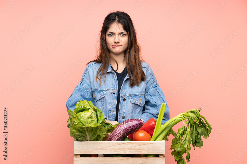 Young farmer woman holding a basket full of fresh vegetables having doubts and with confuse face expression Young farmer woman holding a basket full of fresh vegetables having doubts and with confuse face expression