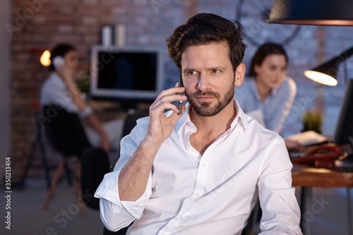 Businessman sitting in office, talking on mobilephone, looking away.